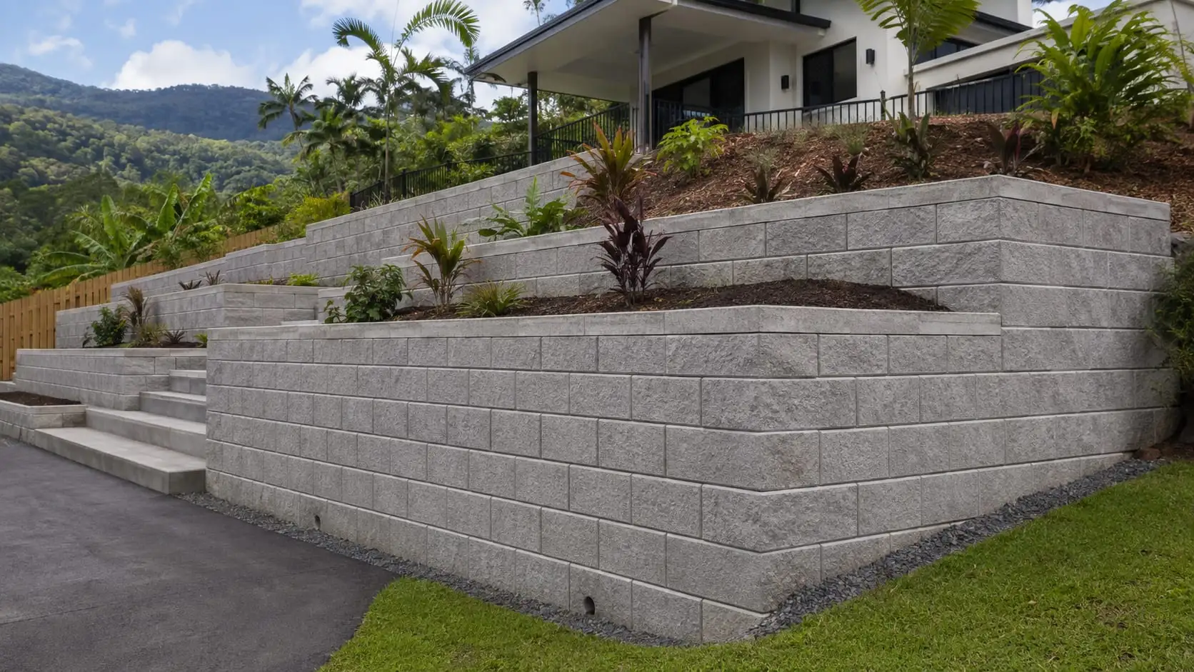 A tiered grey block retaining wall with cast steps running down to a driveway