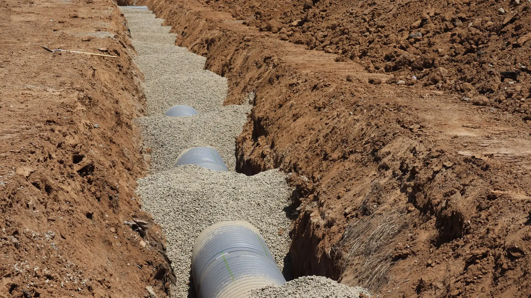 A slotted drainage pipe bedded in gravel in an open trench