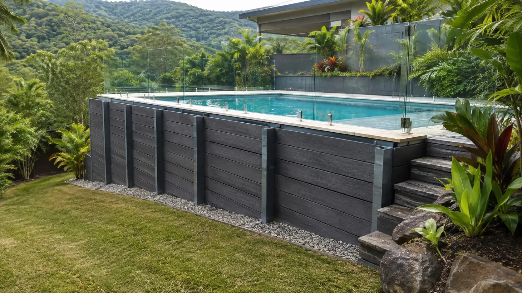 A charcoal sleeper retaining wall carrying the level of a glass-fenced pool